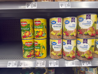 Canned fruit cocktails in grocery aisle.